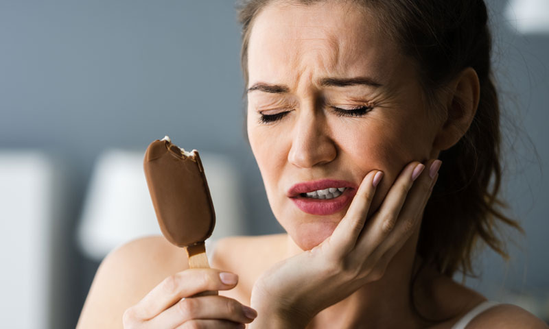 A woman winces in pain as she eats an ice cream bar