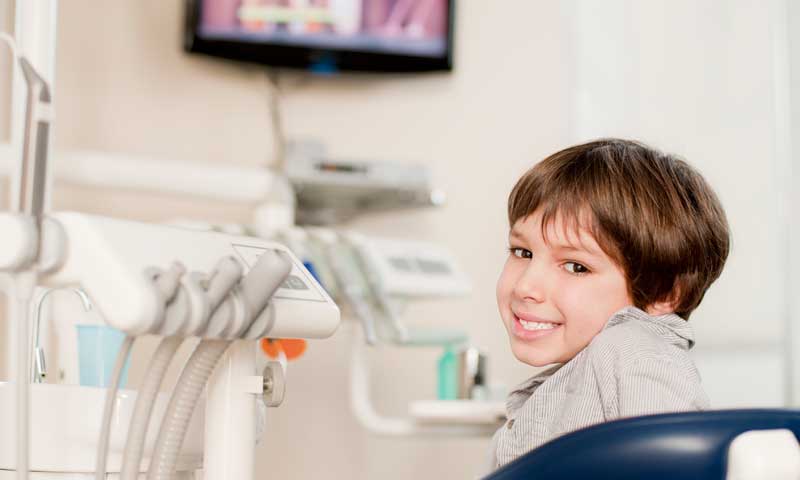A smiling boy watches TV from the dentist’s chair