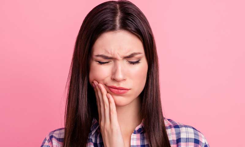 A young woman wincing in pain from impacted wisdom tooth