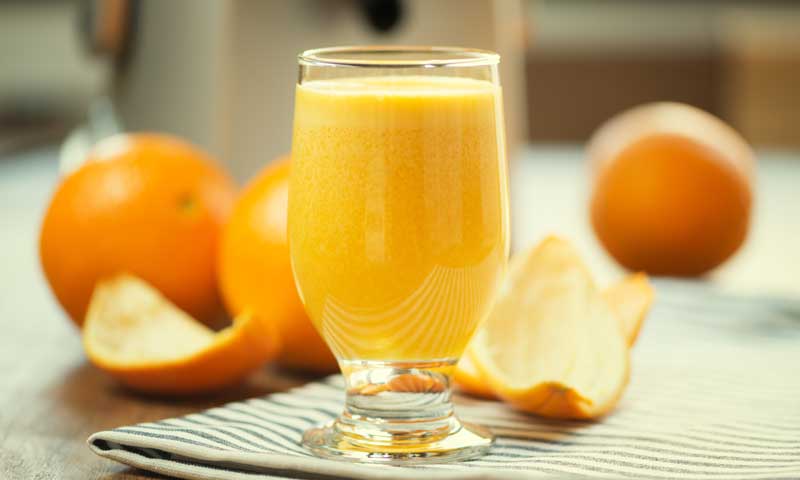 A glass of orange juice surrounded by several oranges