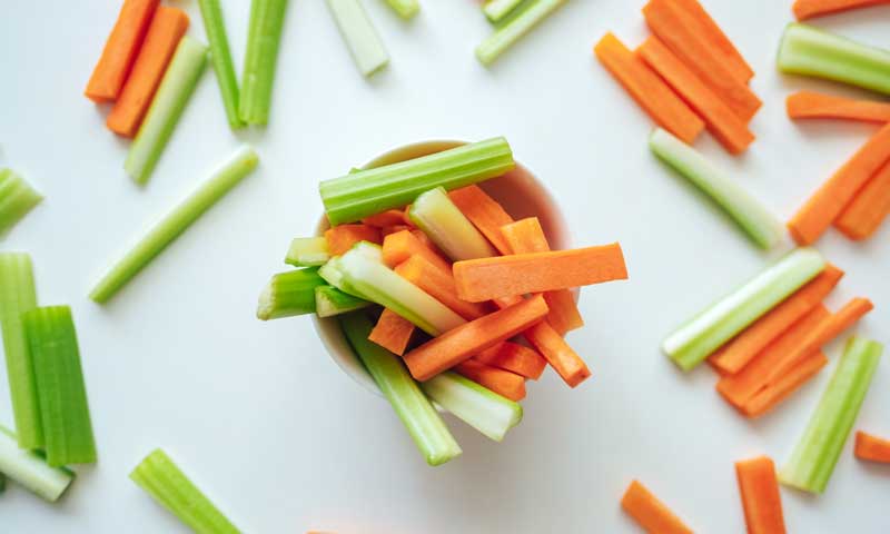 Celery and carrot sticks in a small bowl and on countertop